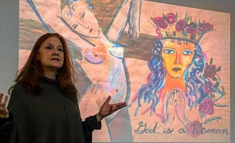Professor Karen Finley stands in front of one of her paintings giving a lecture 